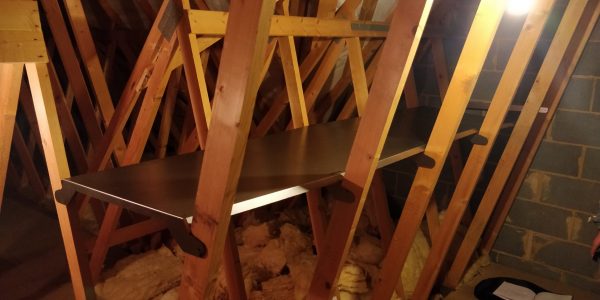 A metal shelf installed between ceiling joists in an attic.