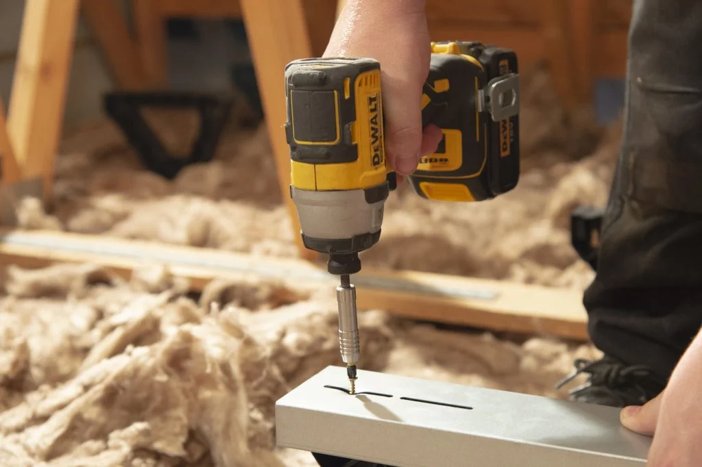 A person using a compact drill to install a floor boarding bracket.