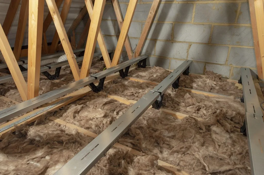 An attic with floor insulation and floor-heightening brackets attached to it.