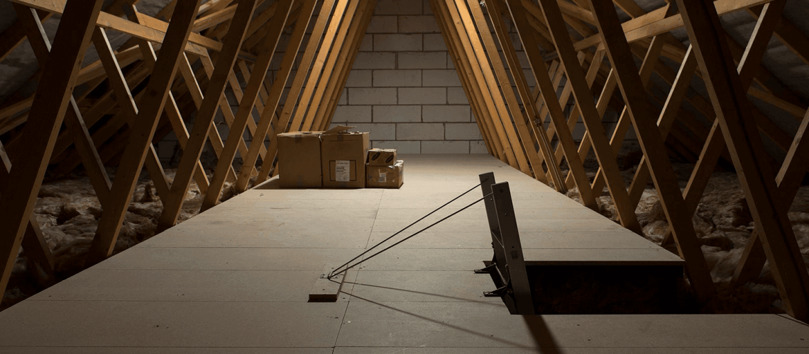 An empty attic with a couple of boxes and an attic hatch with a ladder in the middle.